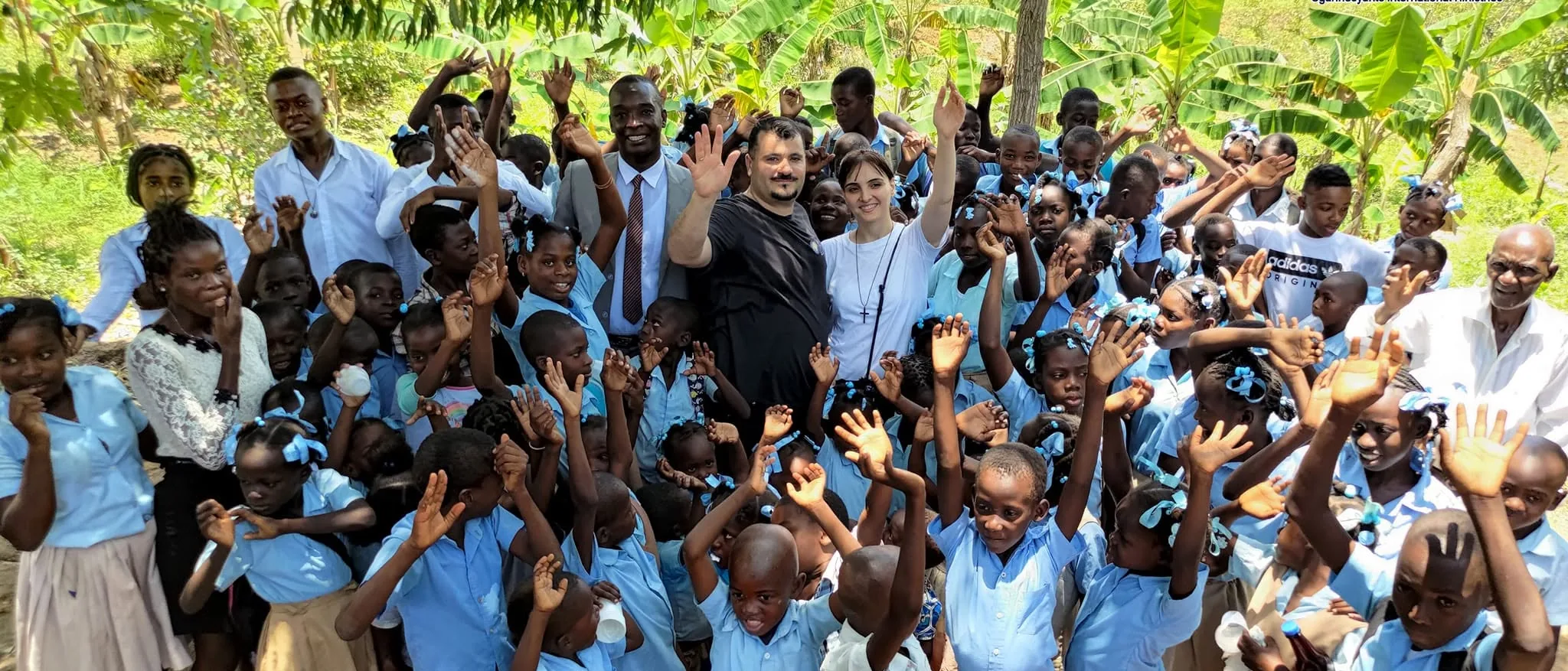 Des enfants saluent la caméra devant l'école soutenue par OIM en Haïti
